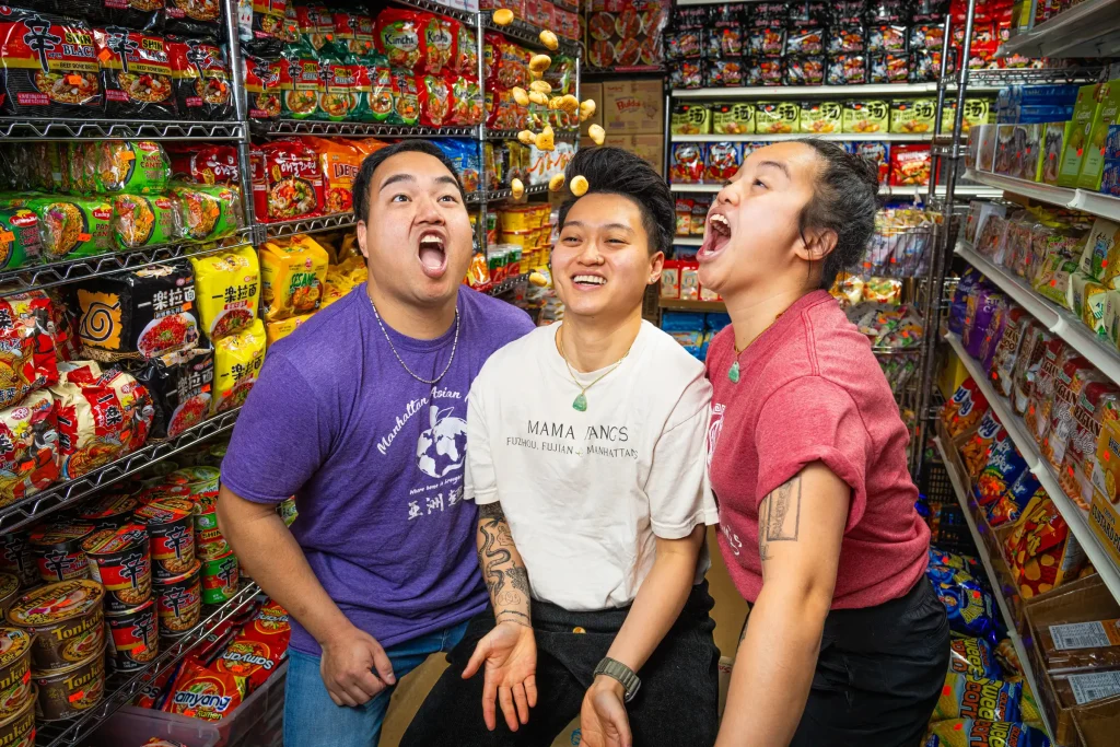 Three friends share a joyful moment surrounded by a colorful assortment of snacks in a vibrant store.