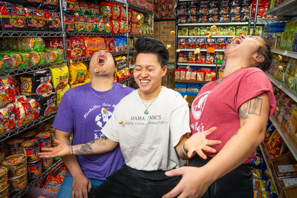 Three friends sharing a hearty laugh in an aisle surrounded by colorful snack packages.