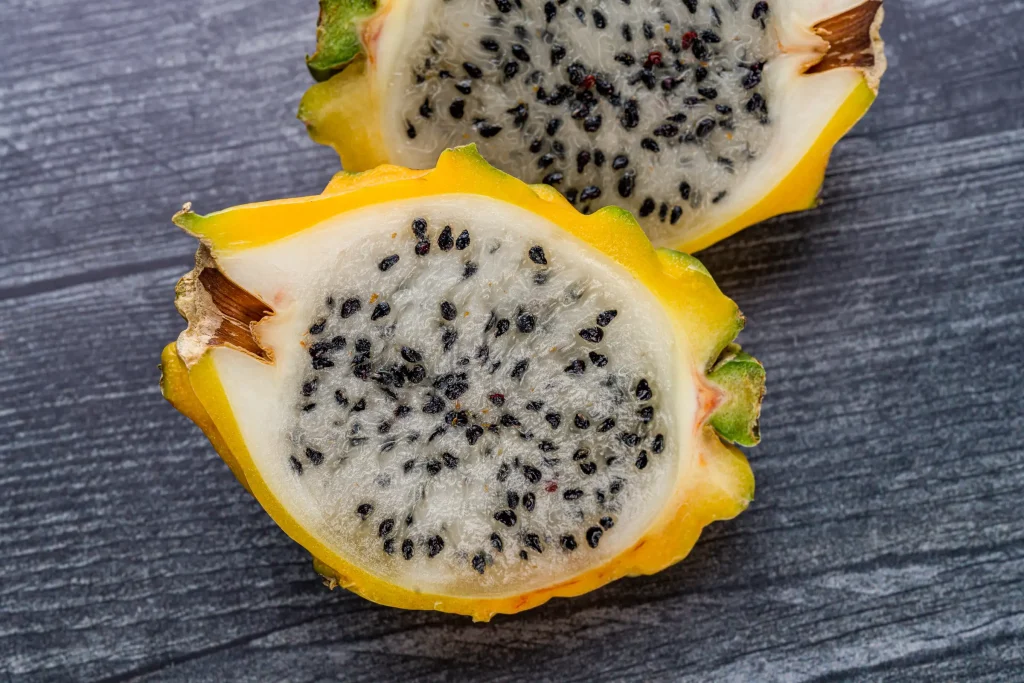 Two halves of a yellow dragon fruit with black seeds, sliced and placed on a wooden surface.
