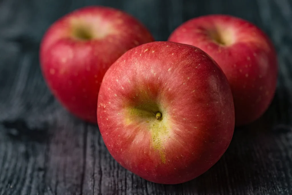 Three red apples on a dark wooden surface.