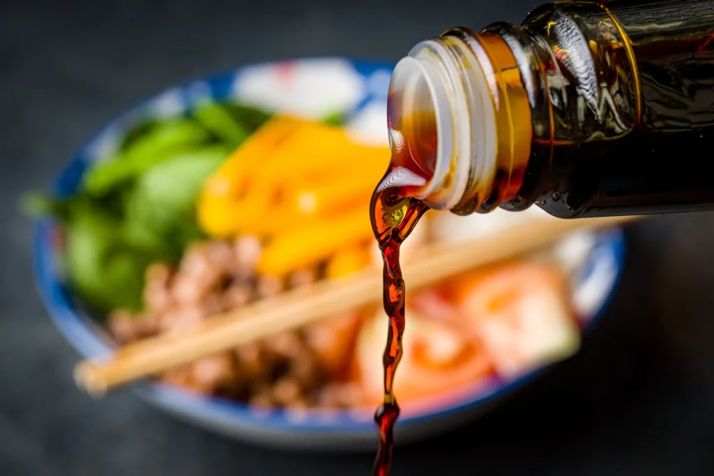 Pouring soy sauce over a bowl of vegetables and protein.