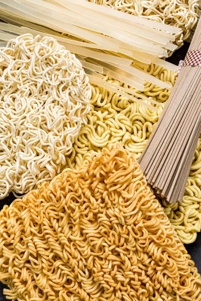 Assorted uncooked noodles and pasta varieties arranged side by side.