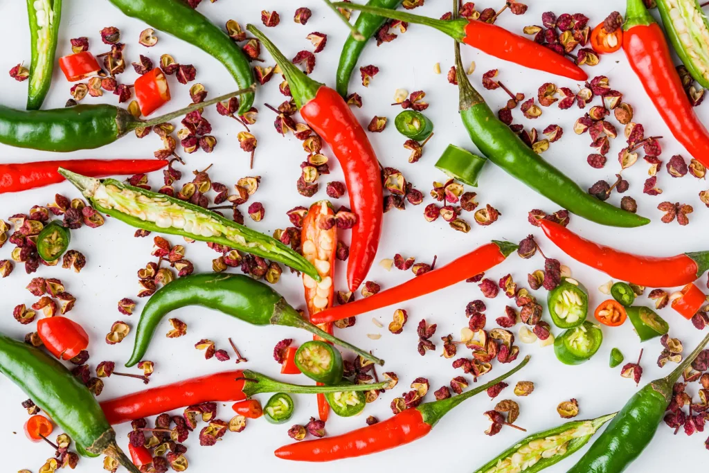 Assorted fresh and dried chili peppers scattered on a white surface.