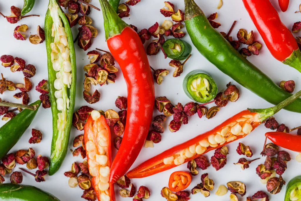 Various whole and sliced chili peppers with seeds scattered on a white background.