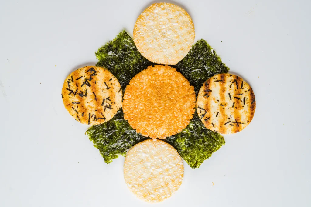 Assorted rice crackers and seaweed snacks arranged in a circular pattern on a white background.