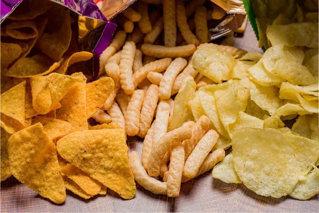 Assorted snack chips spilled from their bags onto a wooden surface.