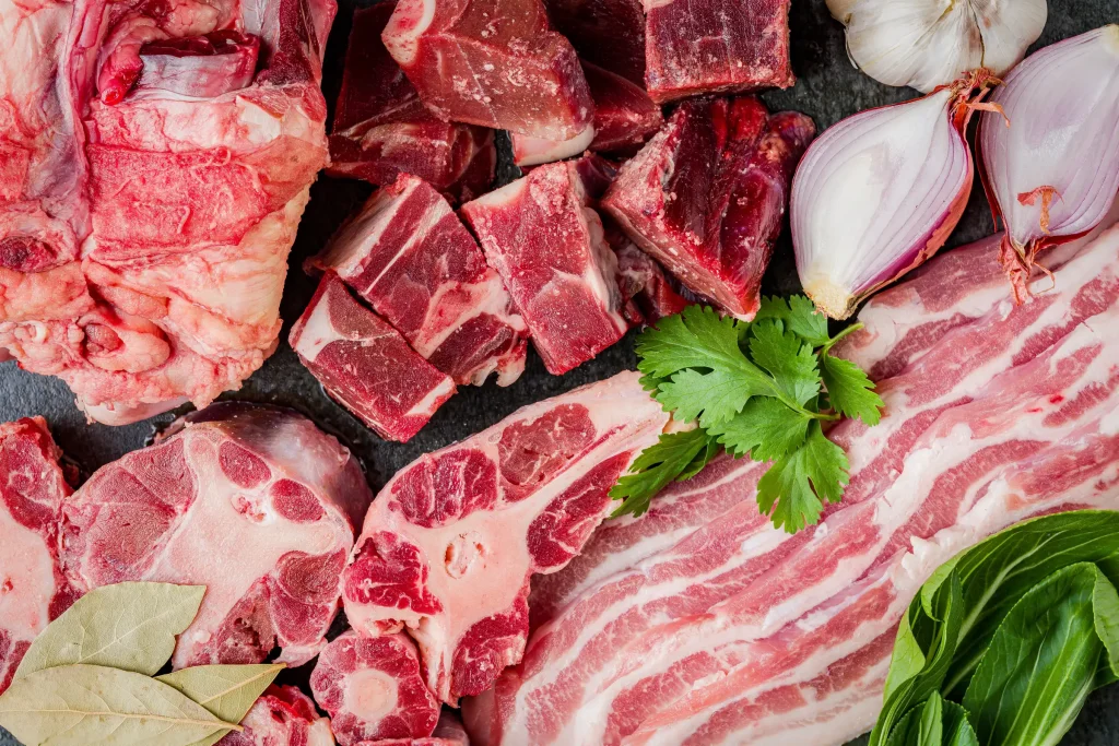 Various cuts of raw meat with herbs and garlic on a slate surface.