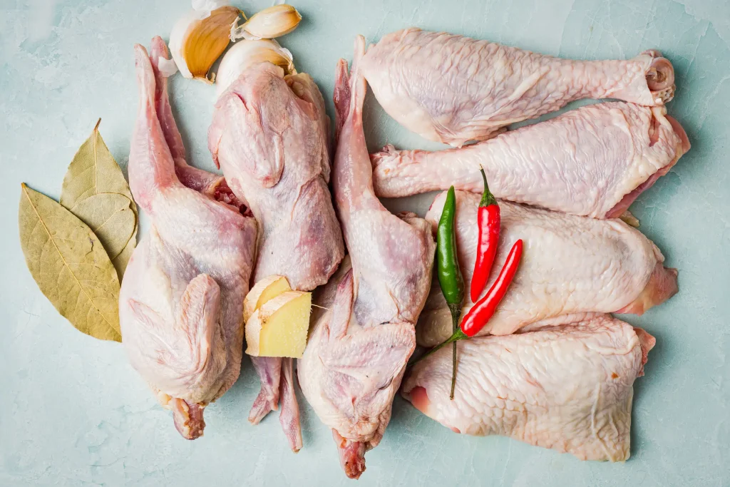 Raw chicken pieces with herbs and spices on a light surface.