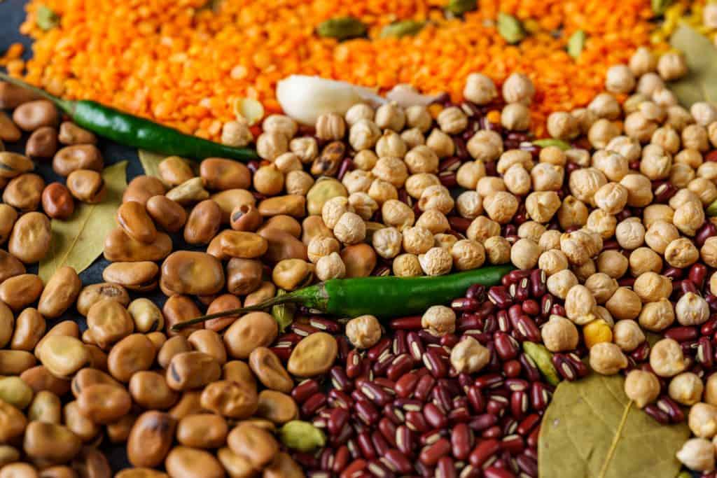 Assortment of beans and spices, including green chilies, bay leaves, and cloves, on a textured surface forming a colorful mosaic of nutritious ingredients.