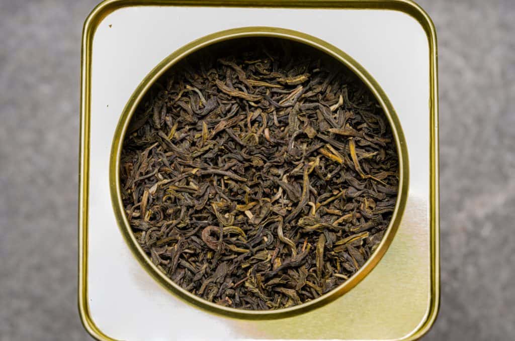 A top view of a container filled with loose black tea leaves, displaying their natural twists and textures, ready to be steeped into refreshing beverages.