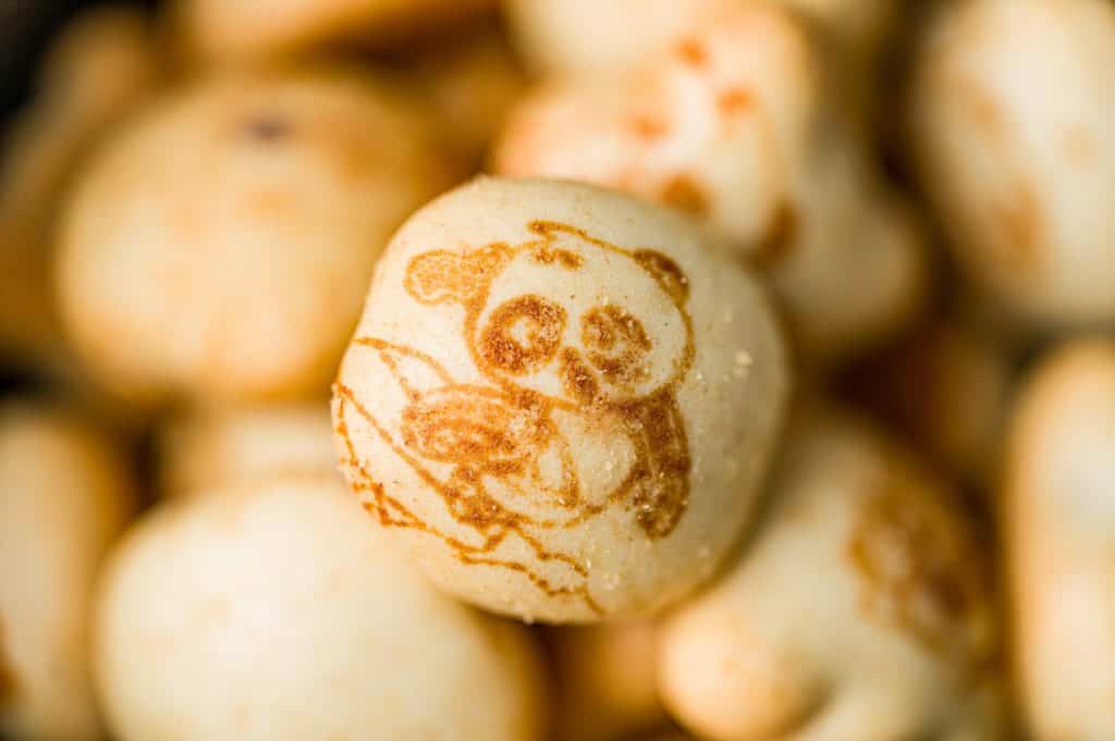 Close-up of a delightful snack: a cookie with an adorable panda face design on top, amidst a pile of similar snacks.