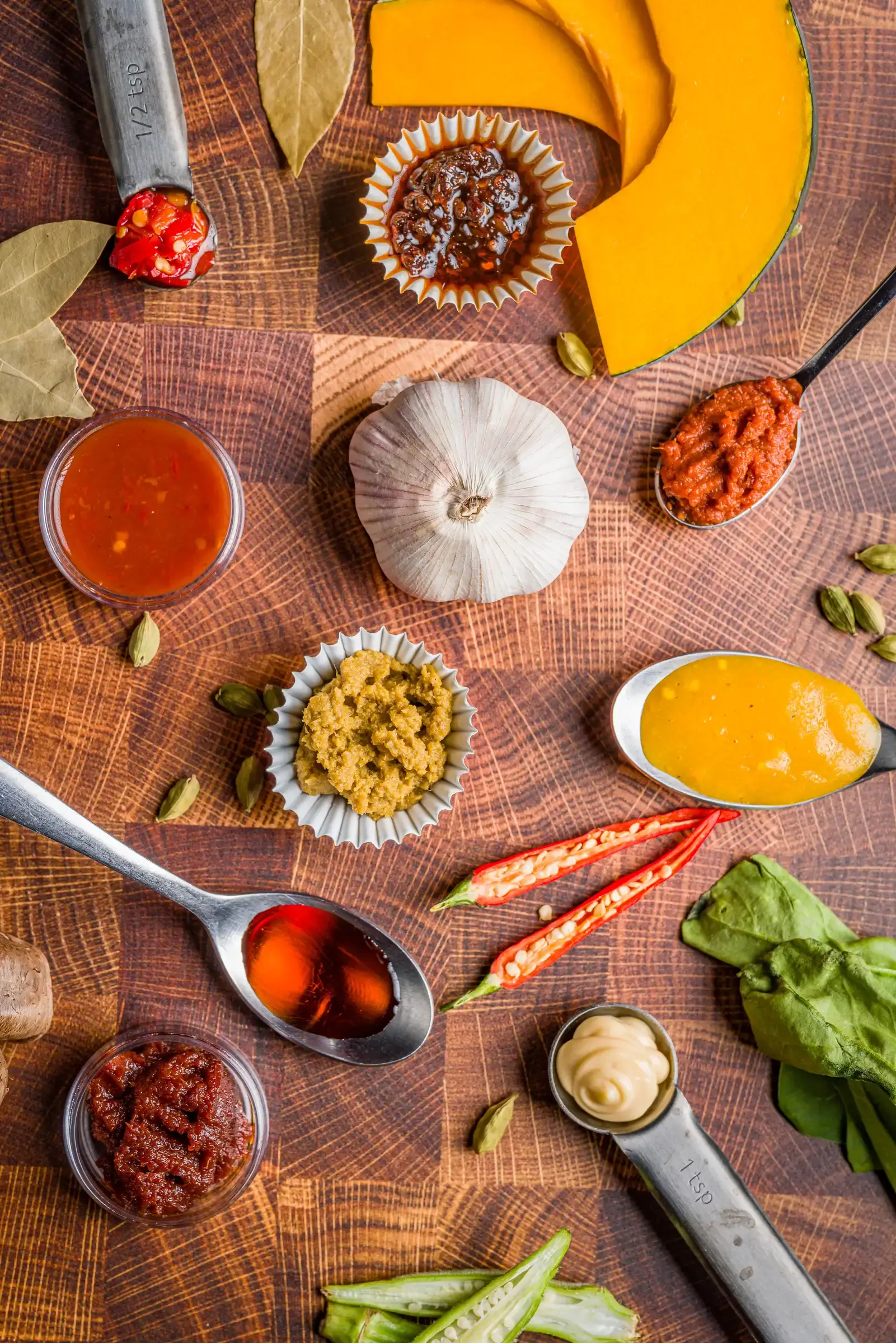 Various ingredients and spices, including chili peppers, garlic, and pumpkin, neatly arranged on a wooden surface.