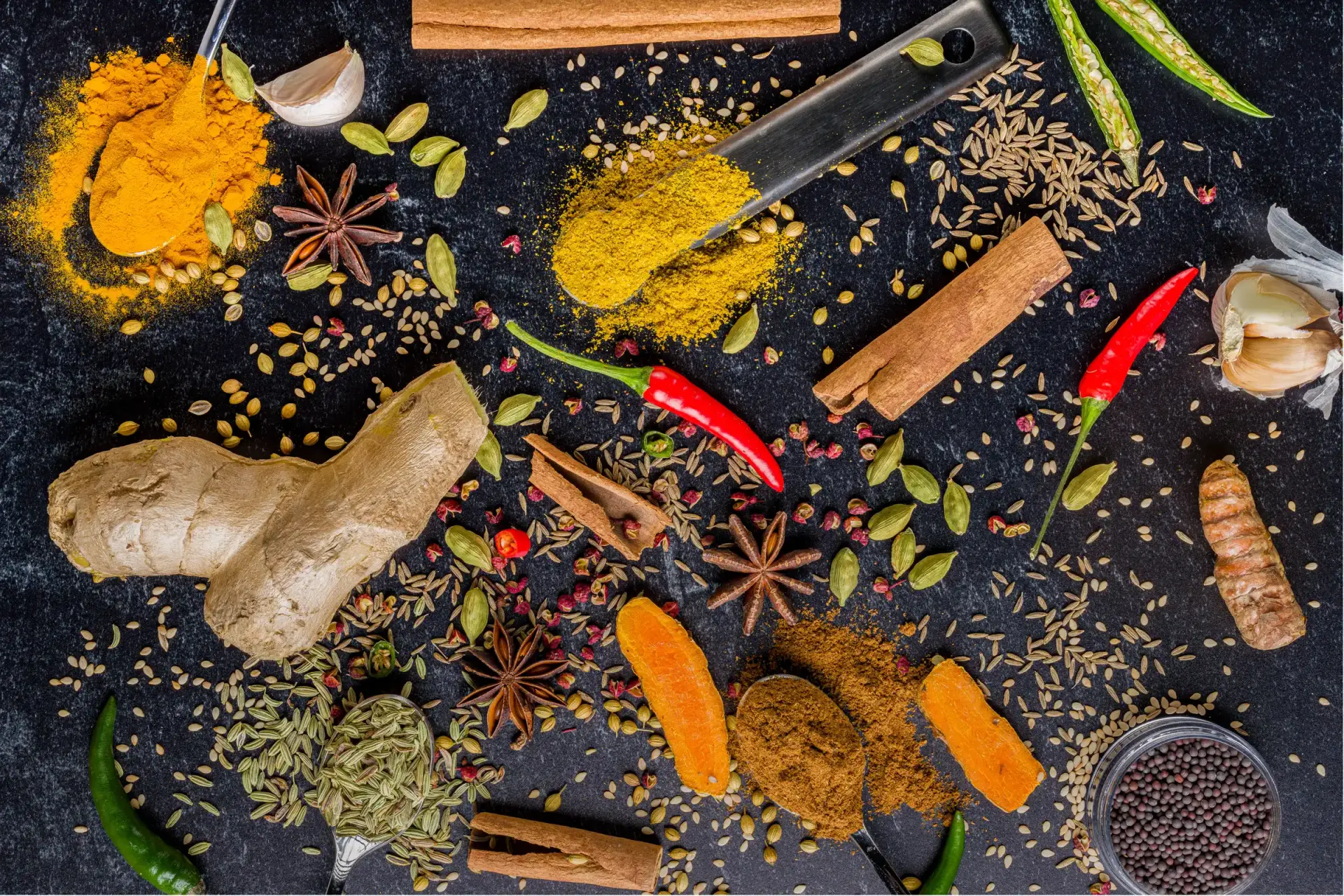 Assortment of colorful spices and herbs scattered on a dark surface.
